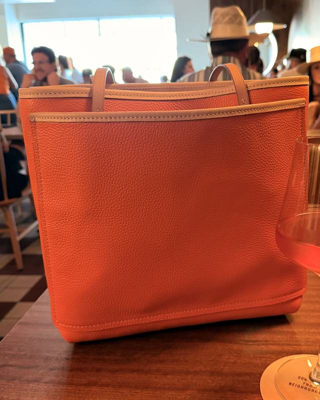 Bigger Bag, a persimmon pebbled leather tote, on a restaurant table