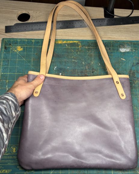 Normal Bag, a lavender leather tote, held up on a workbench